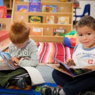 Two children sitting on the floor reading books in a classroom