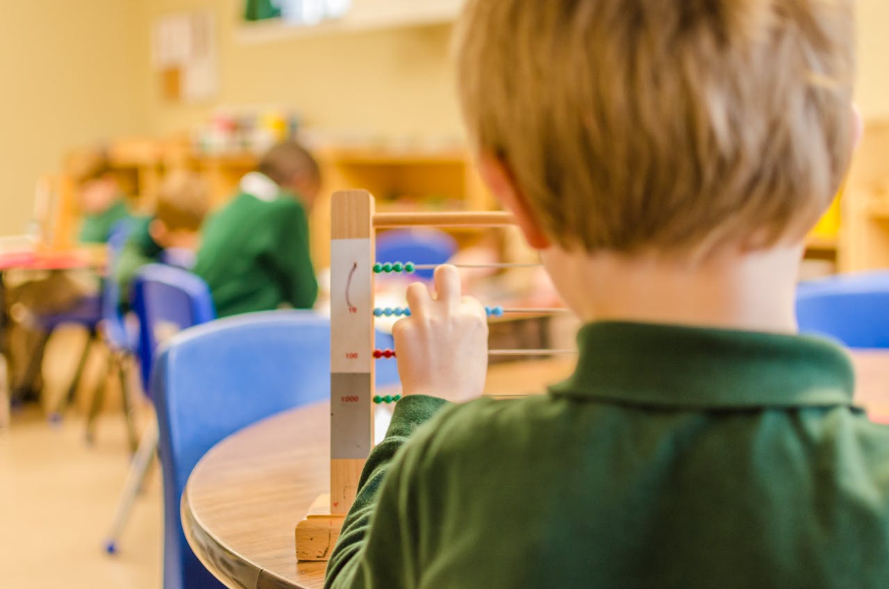Child in green shirt using an abacus in a classroom