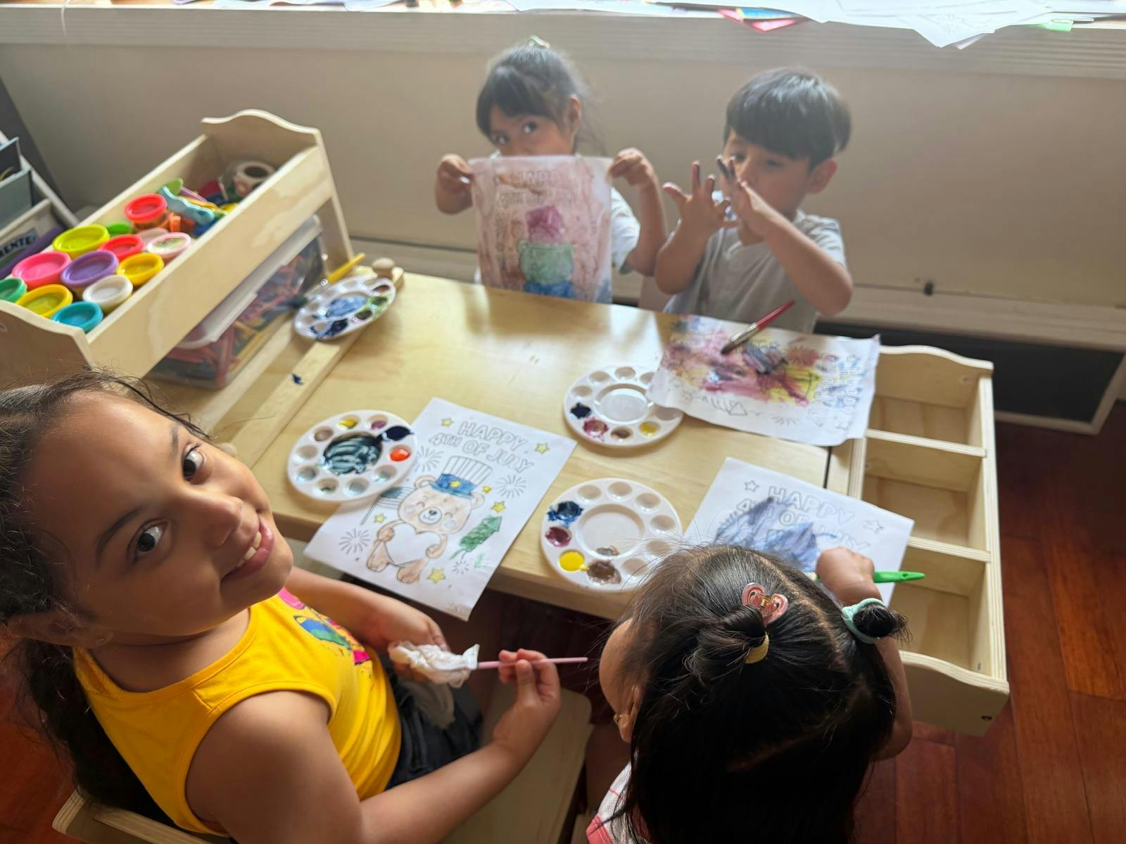 Four children painting at a wooden table