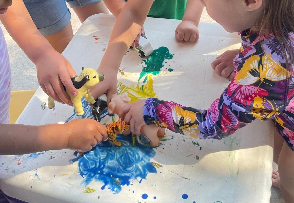 Children playing with paint and animal toys on a table
