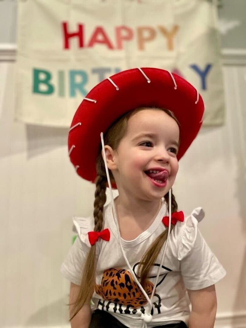 Child in a red cowboy hat with pigtails and red bows, sticking out tongue