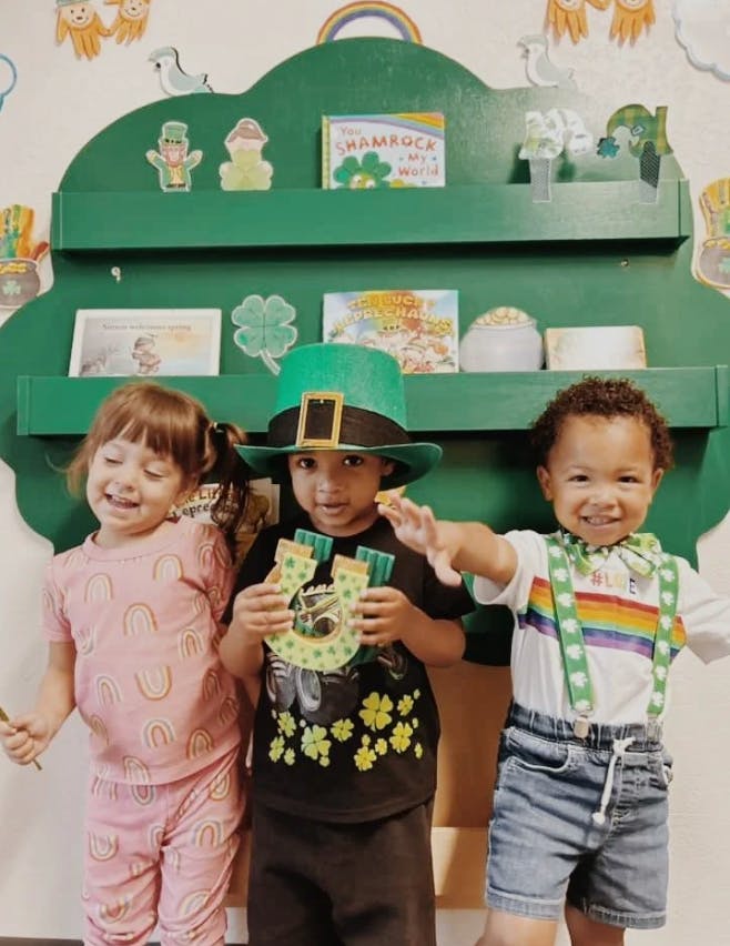 Three children in front of a green shelf with St. Patrick's Day decorations