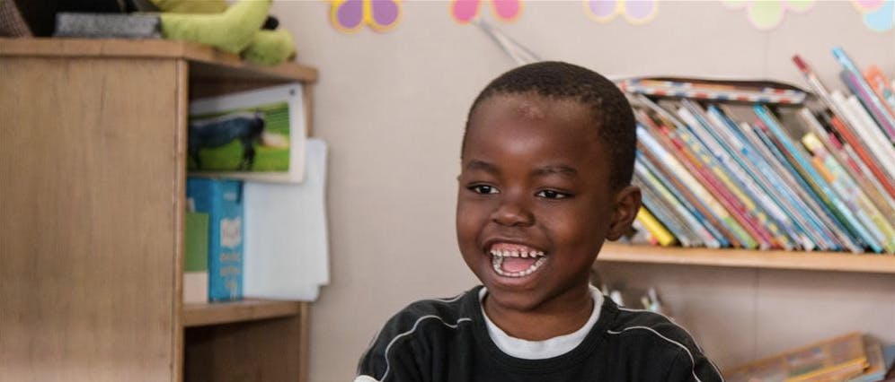 Child smiling with open mouth in a room with bookshelves