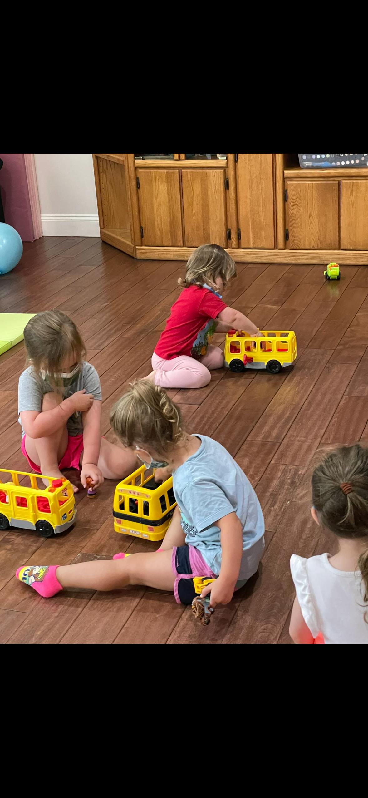 Children playing with toy school buses on a wooden floor