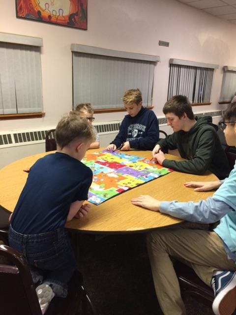 Four teens and a child sitting around a table with a colorful puzzle