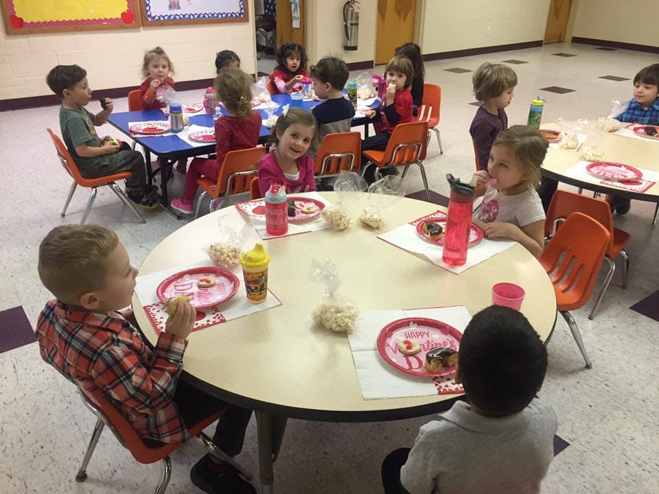 Children sitting at tables eating in a classroom eating snacks
