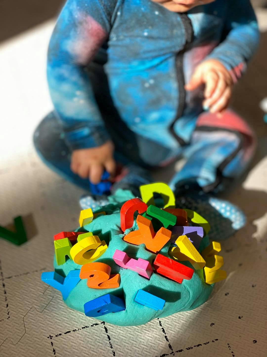 Child playing with colorful letter blocks pushed into turquoise playdough