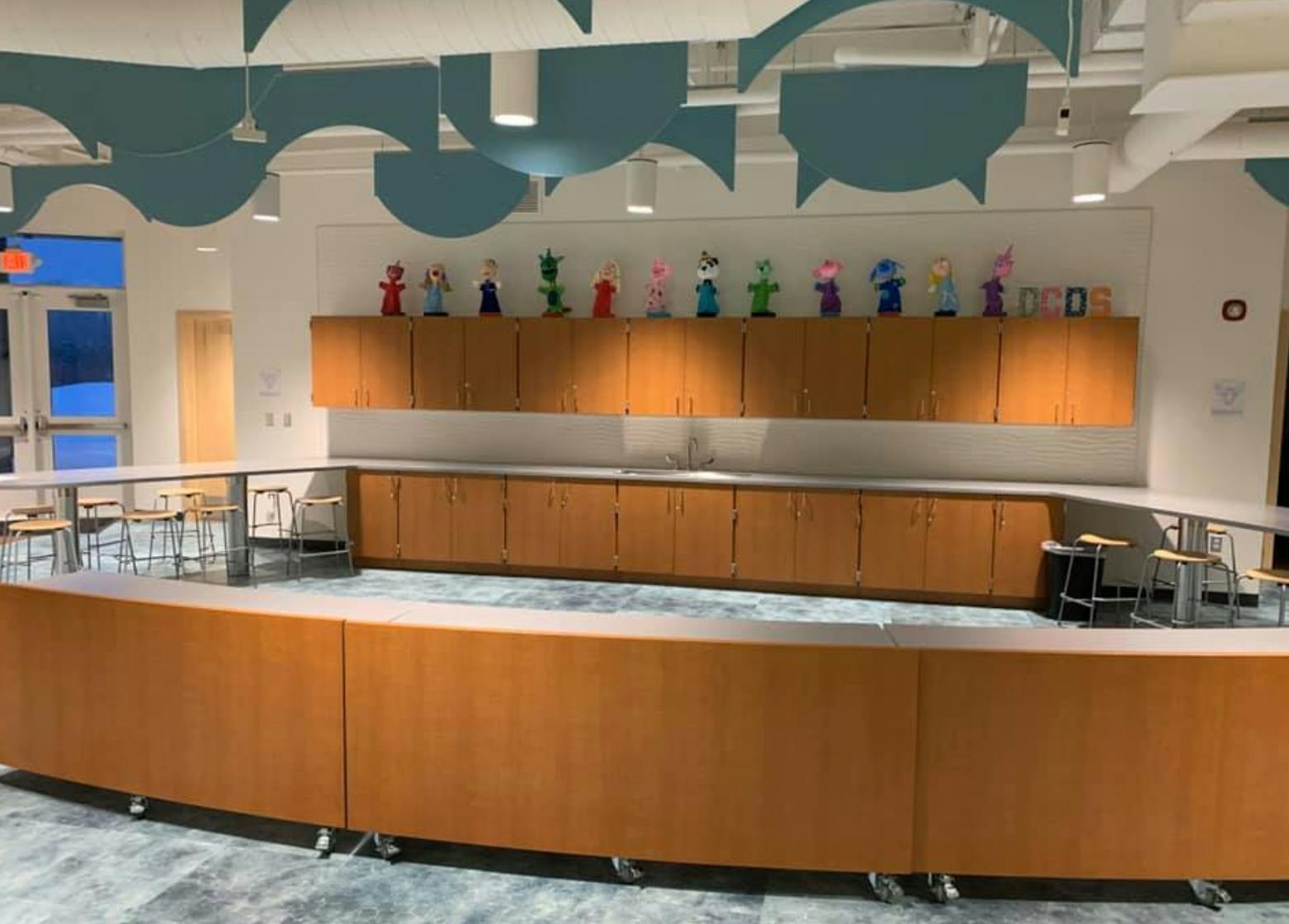 Curved wooden counter with stools in a room with cabinets and colorful figures
