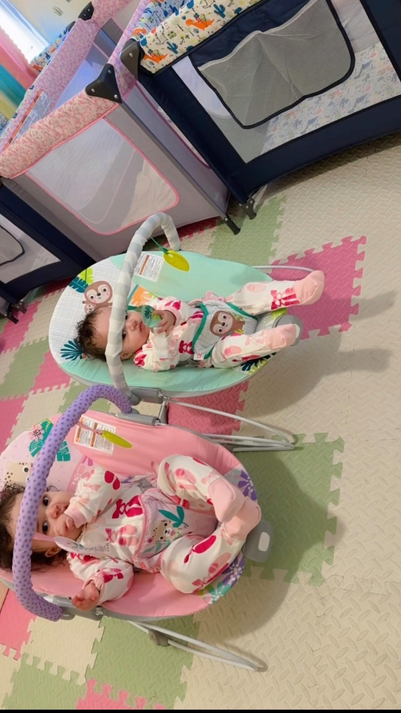 two babies lying in bouncers on a playmat