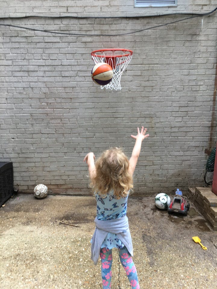 Child reaching for a basketball going through a hoop