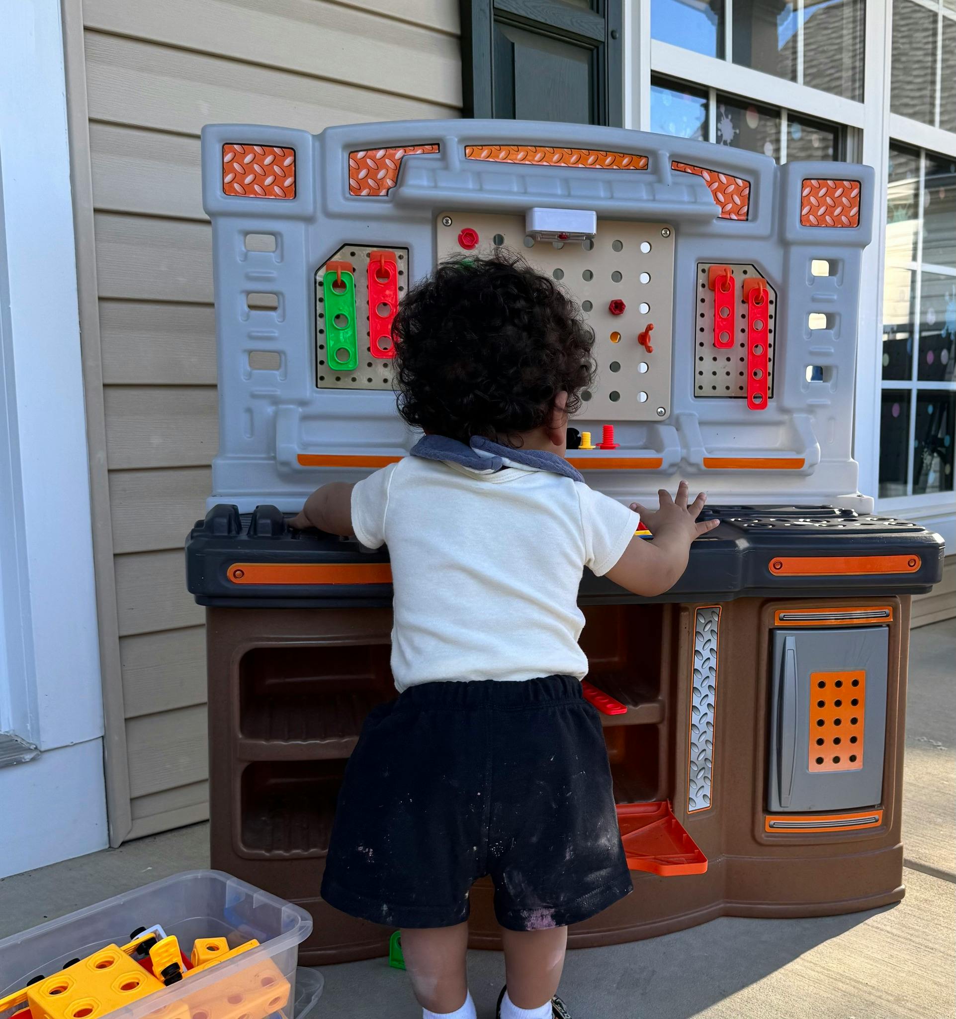 Child standing with their back to the camera, playing with a toy workbench