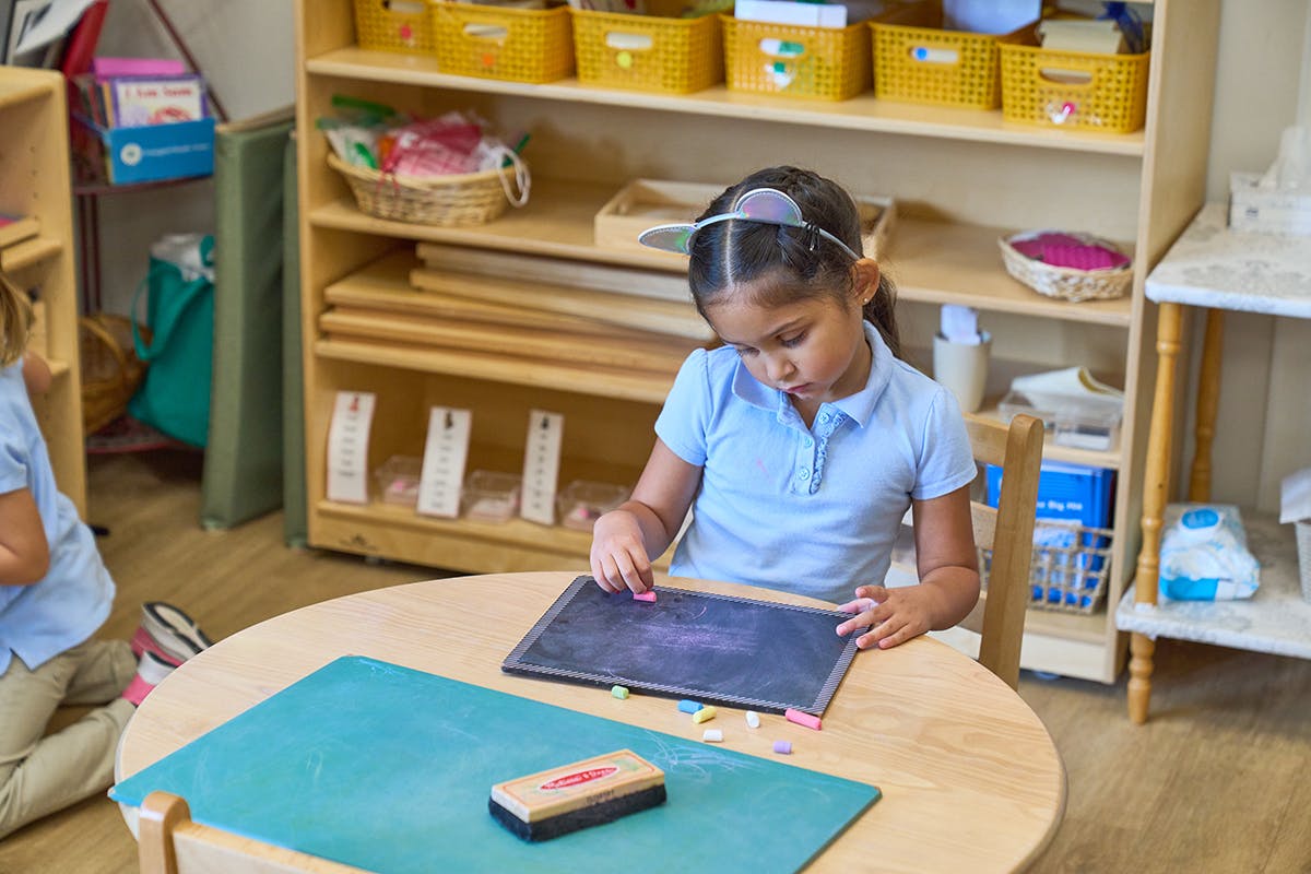 Child writing on a chalkboard at a table in a classroom