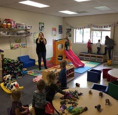 Adults and children in a playroom with toys and a slide