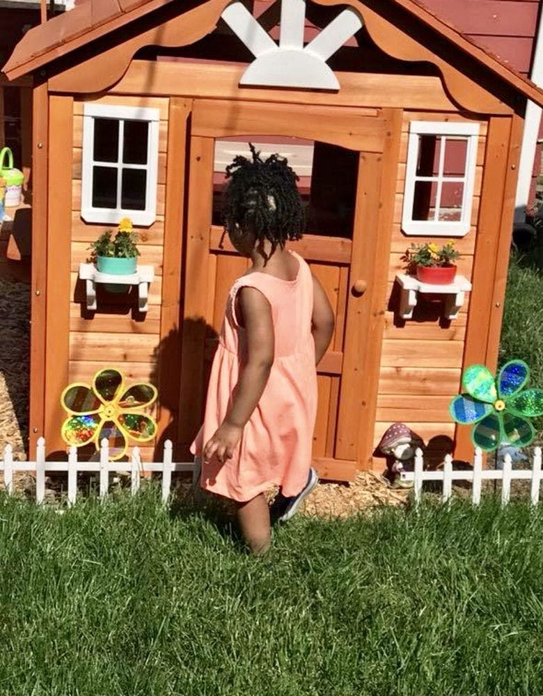 Child standing in front of a wooden playhouse