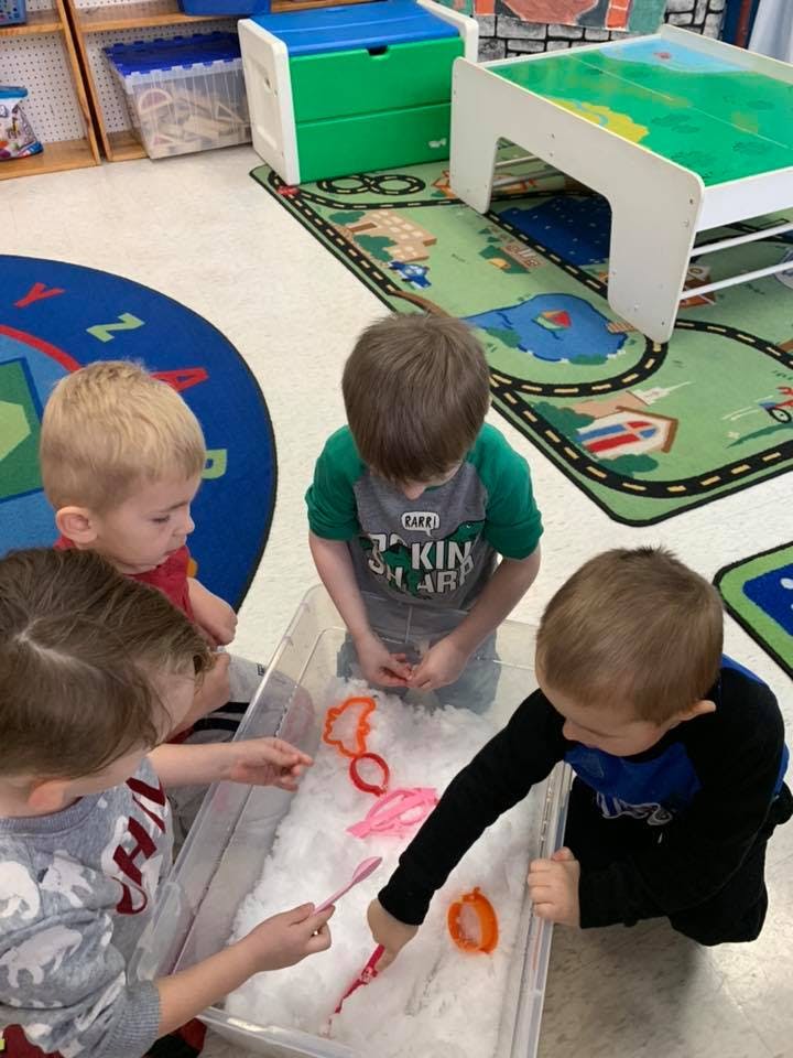 Children playing with sensory bin with white filler and colorful cookie cutters