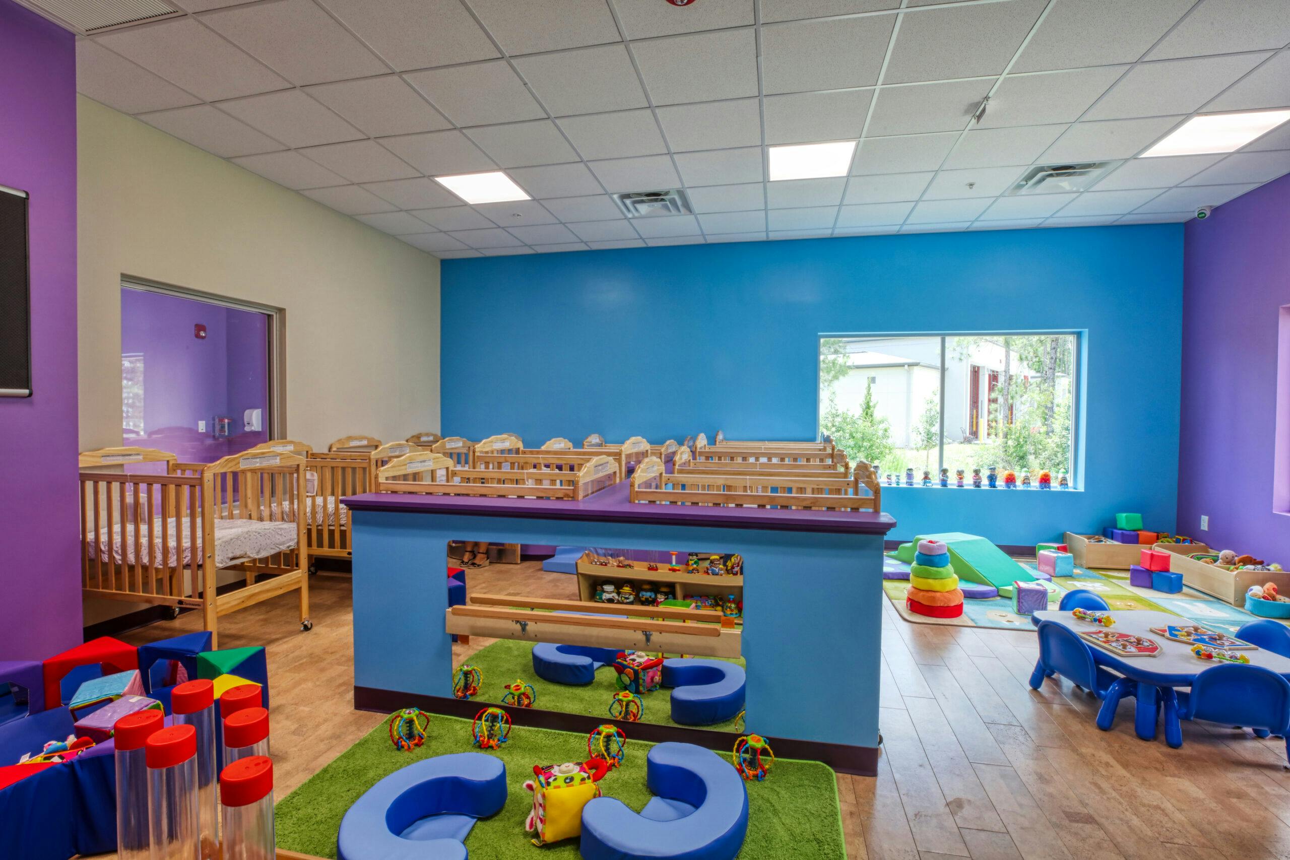 Classroom with multiple cribs and a play area with toys and small furniture