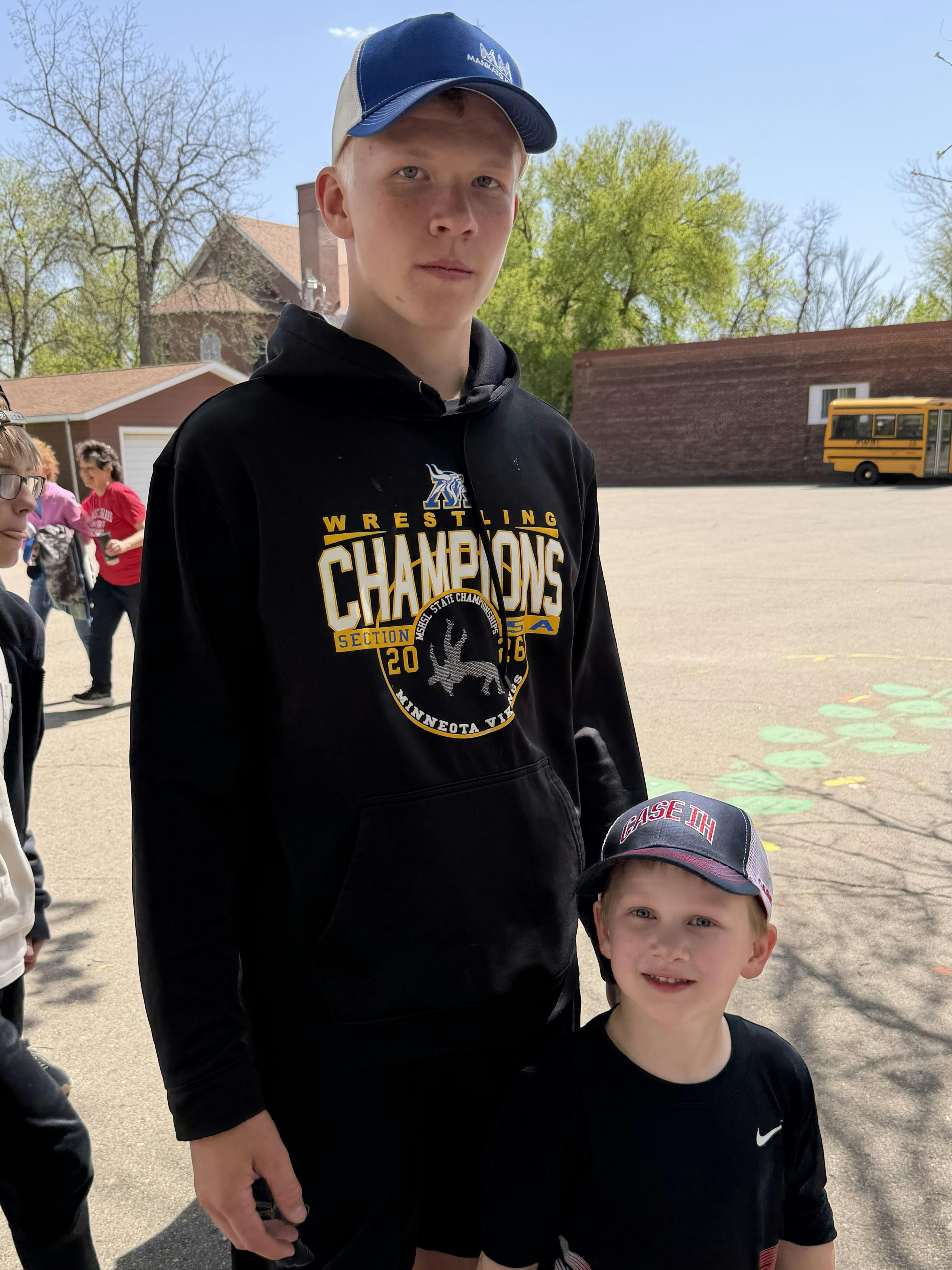 A teen wearing a wrestling hoodie and a child wearing a baseball cap standing