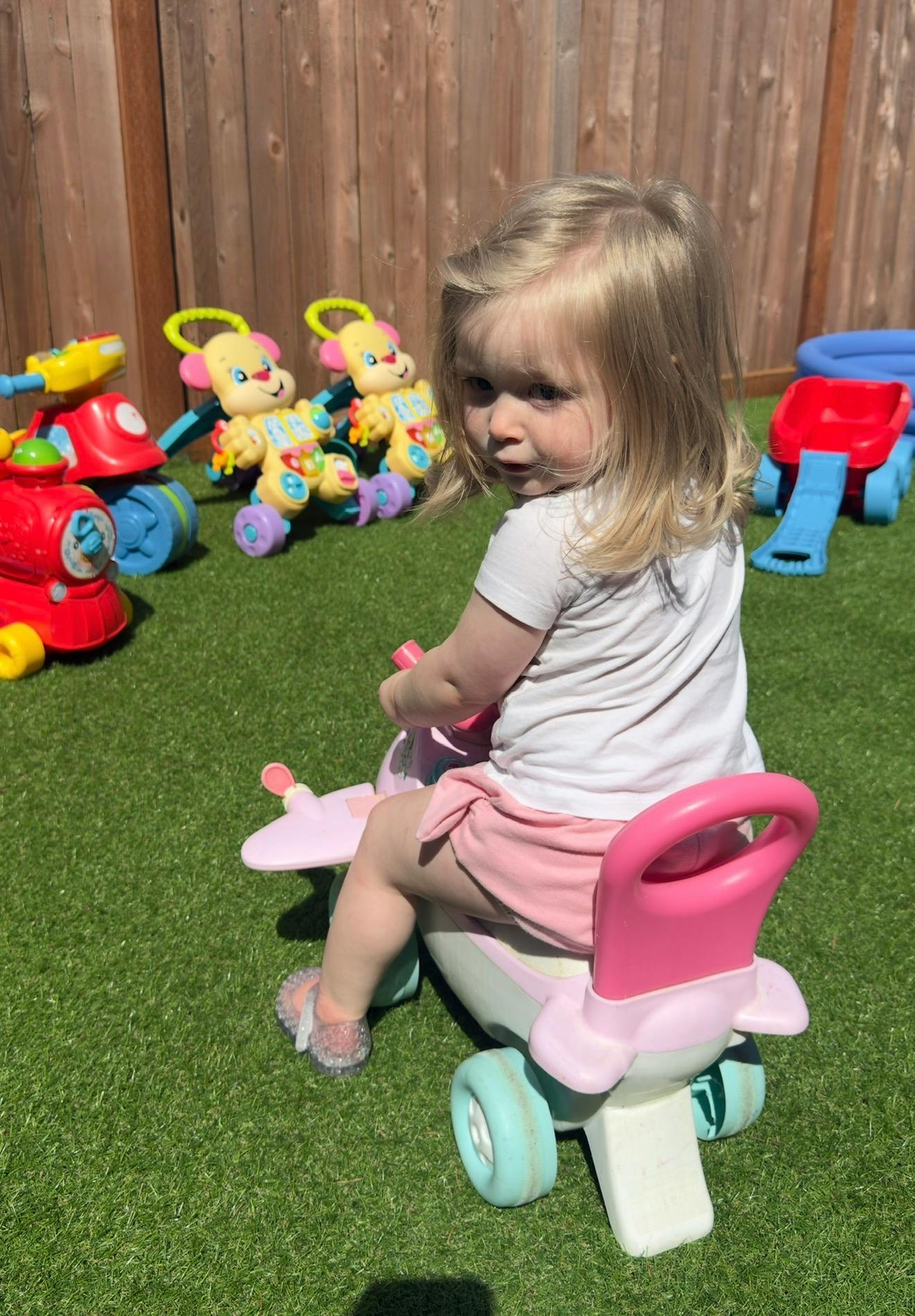 Child riding a toy on artificial grass surrounded by other toys