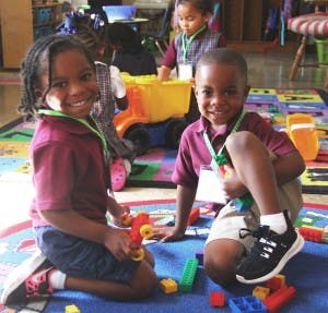Two children kneeling on a rug with building blocks
