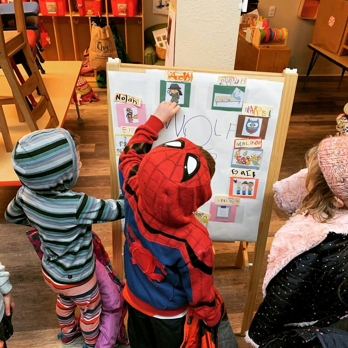 Child in Spider-Man costume pointing at a board with another child nearby