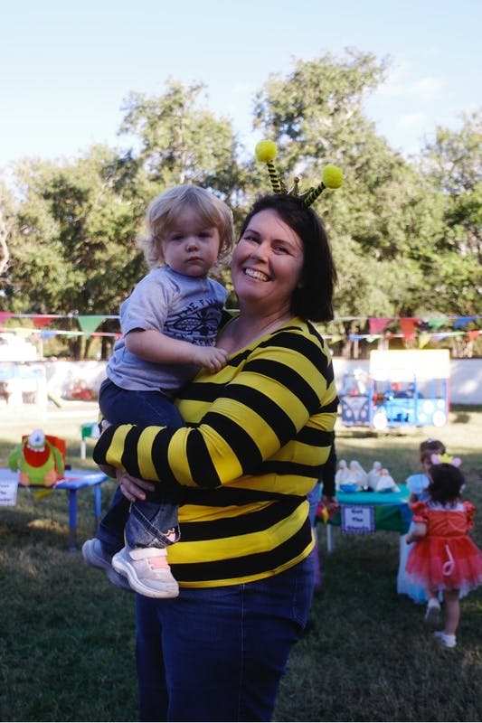 Adult wearing a bee costume holding a child outdoors
