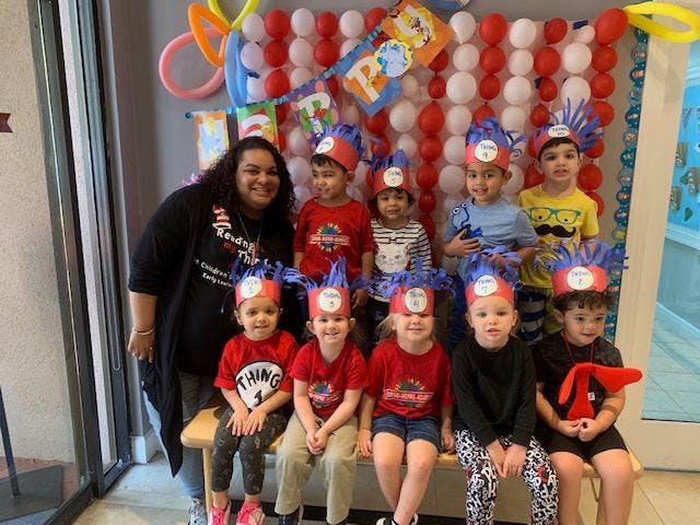 Person with a group of children wearing hats in front of a balloon wall