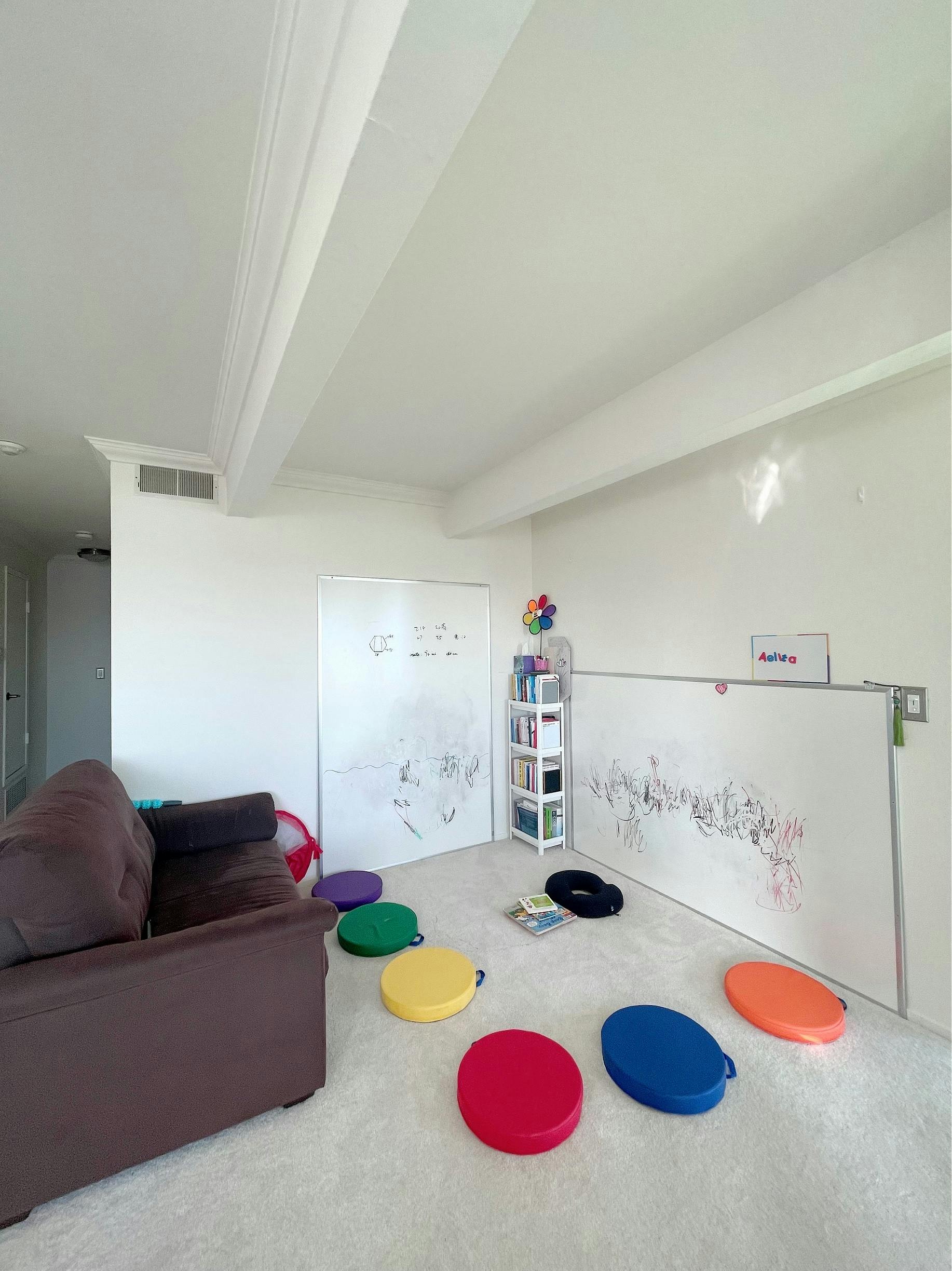 Living room with a brown couch, whiteboards, and colorful floor cushions