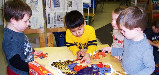 Four children playing with puzzles at a table