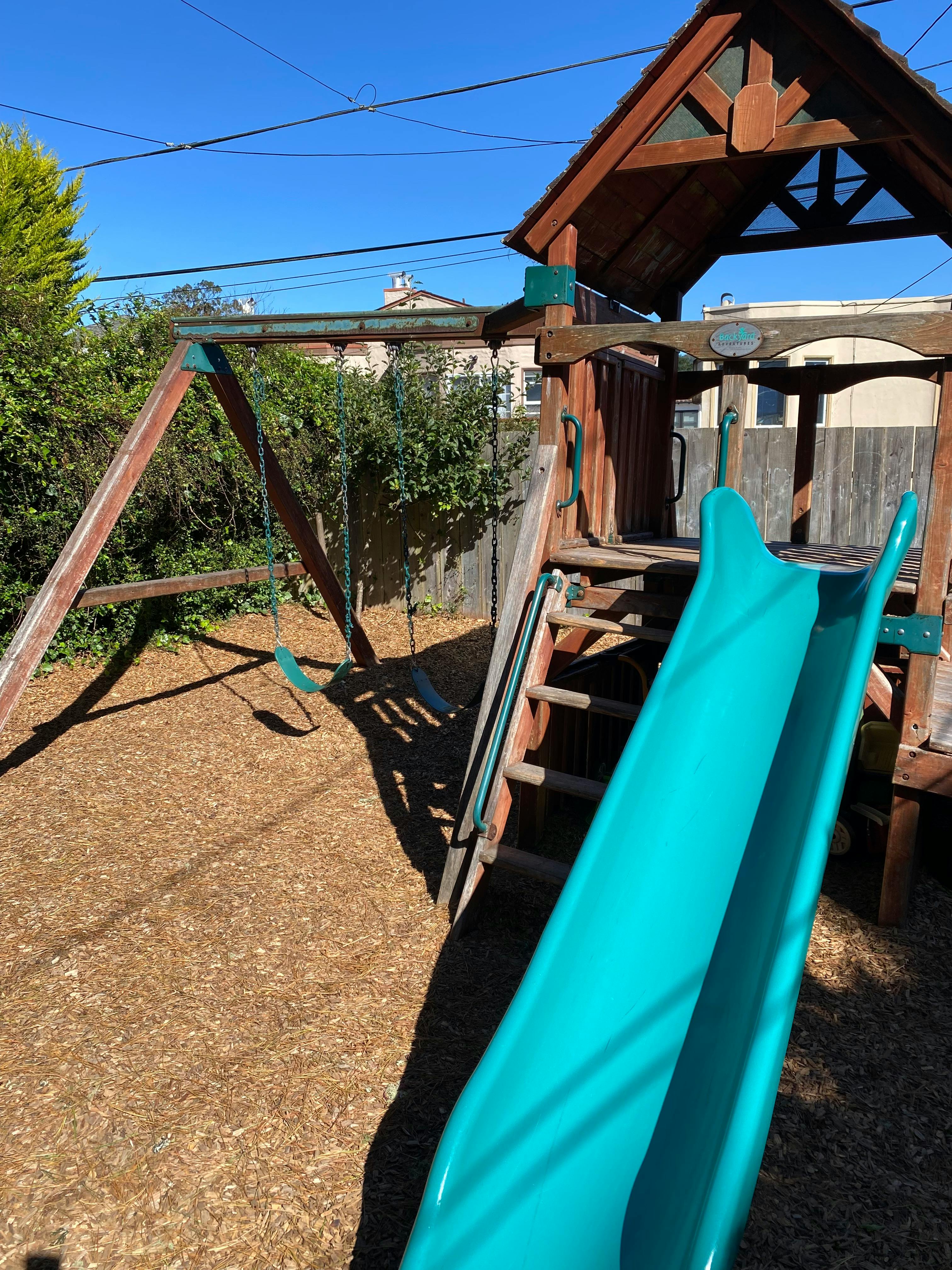Playground with a wooden swing set and a blue slide