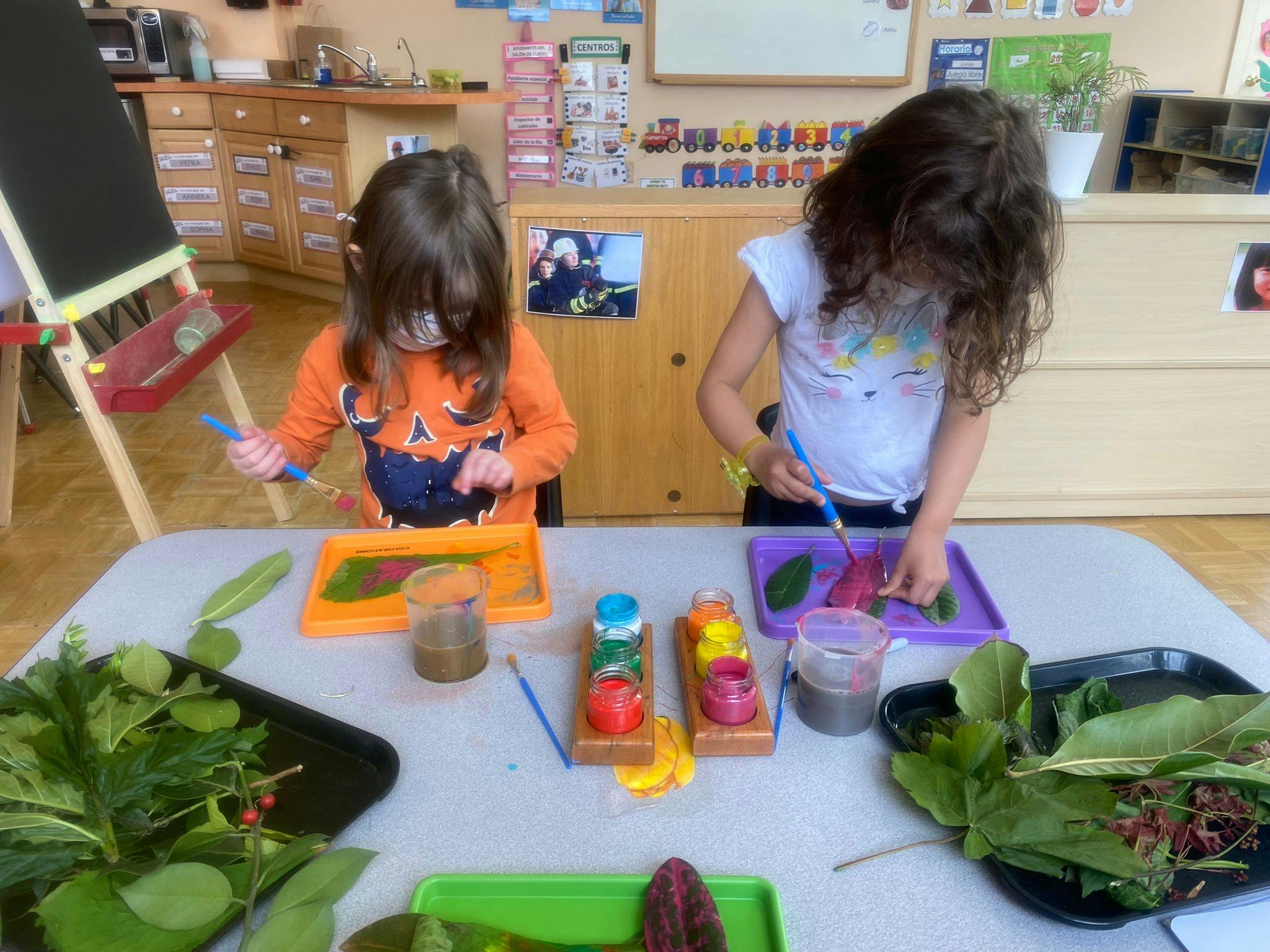 Two children painting leaves at a table