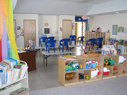 Classroom with tables, blue chairs, and shelves with toys and books