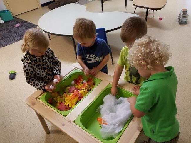Four children playing at a sensory table with colorful objects and white fluff
