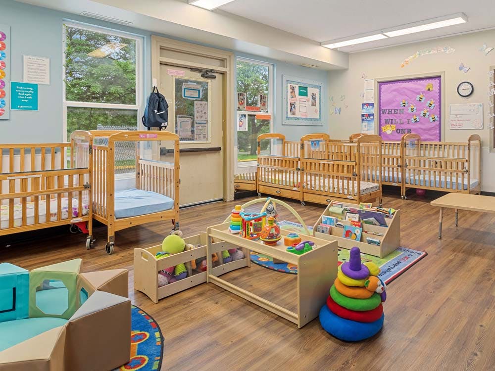 Cribs and toys in a daycare room with windows and a purple door