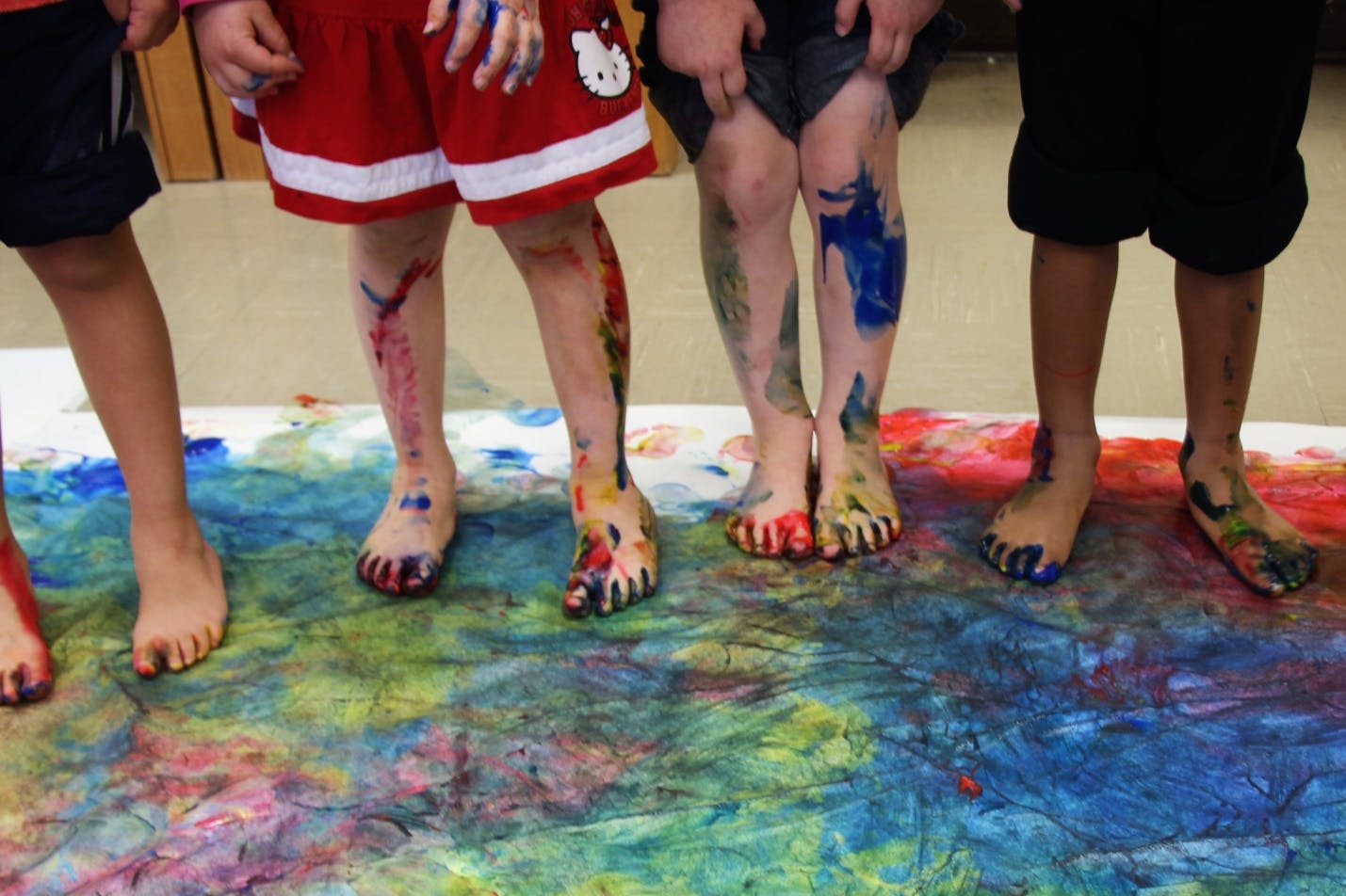 Children's legs and feet covered in paint standing on a painted surface