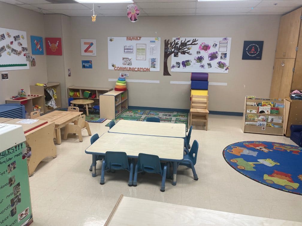 An empty classroom with small tables and chairs, shelves, and a rug