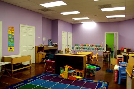 Empty classroom with purple walls, small tables, chairs, and toys