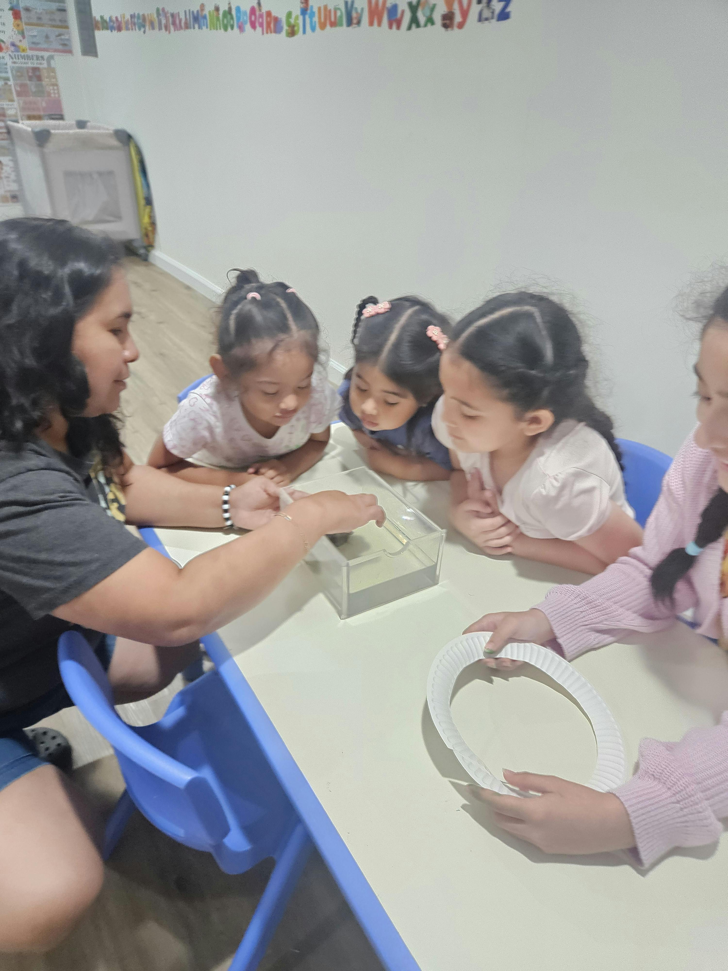 A person and three children working with a container on a table