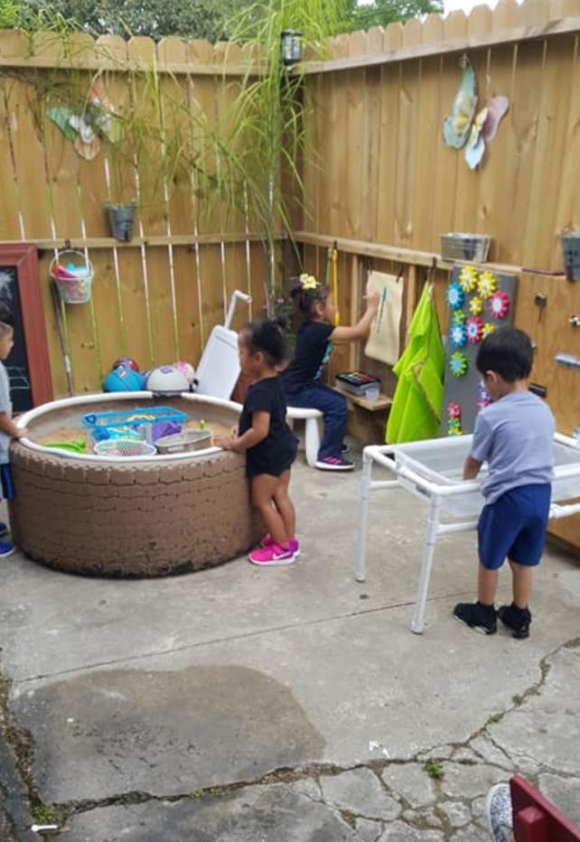 Children playing in an outdoor area with a sandpit and activity stations