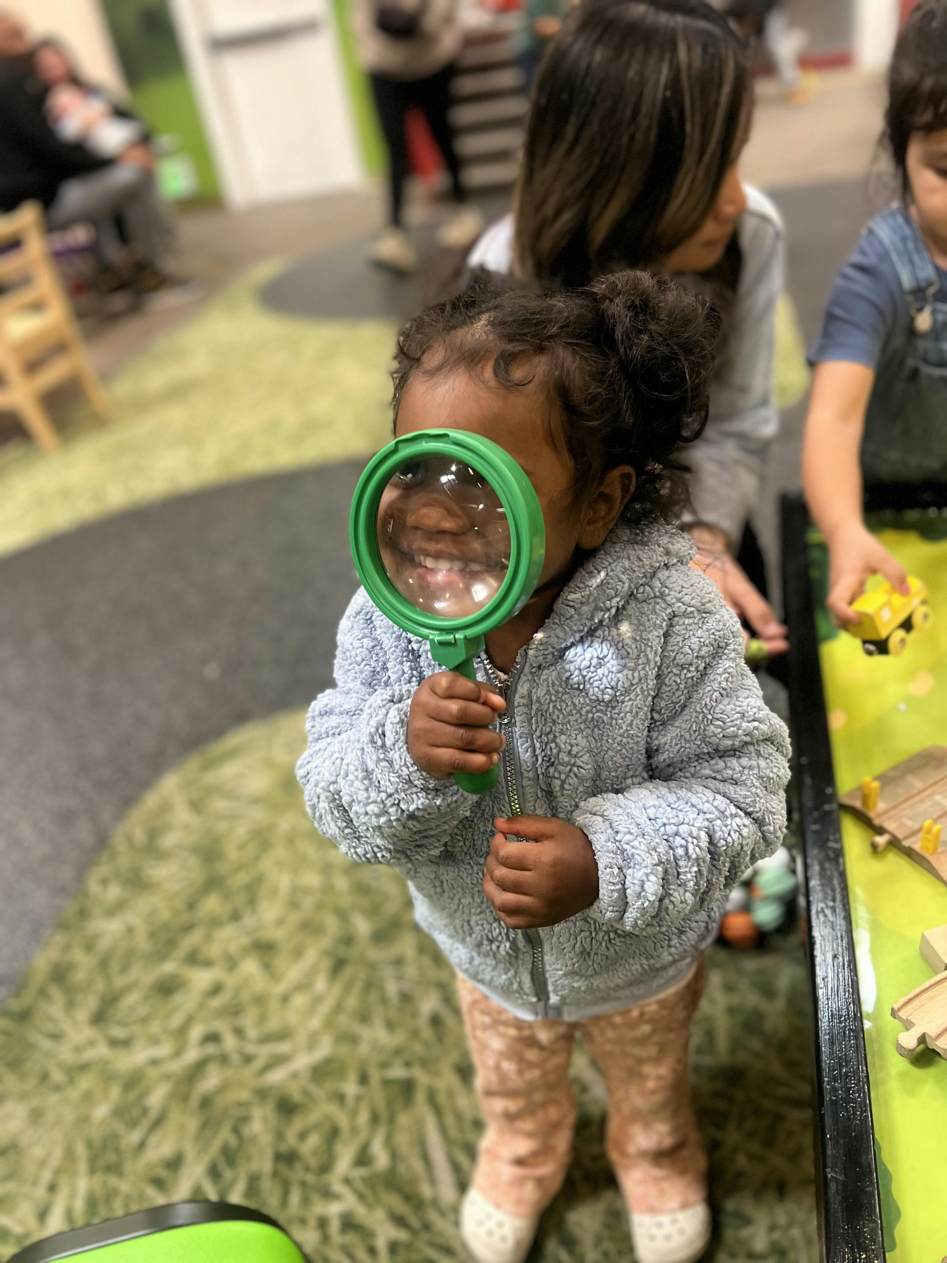 Child holding a green magnifying glass to their face