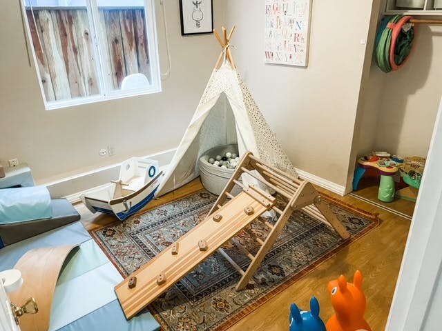 Indoor play area with a teepee, wooden slide, and boat-rocker boat