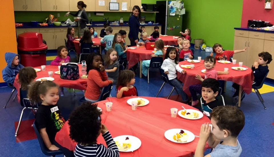 Children sitting at tables with plates in a classroom