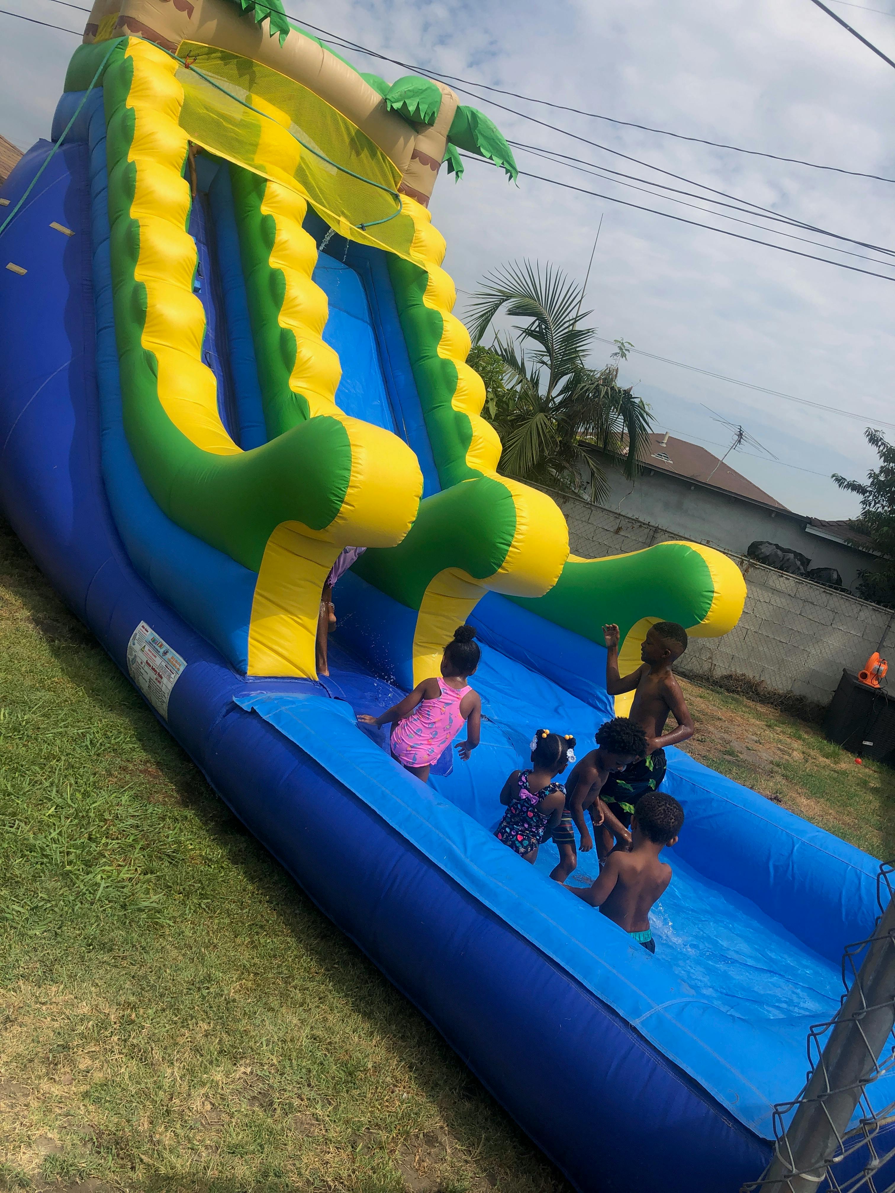 Several children playing on a large blue, green, and yellow inflatable water slide