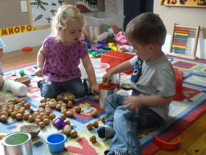 Two children playing with nuts and containers on a rug