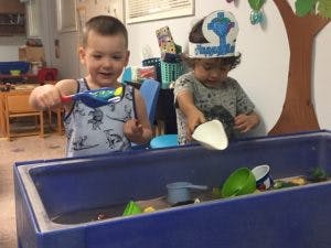 Two children playing with sand and toys in a sensory bin