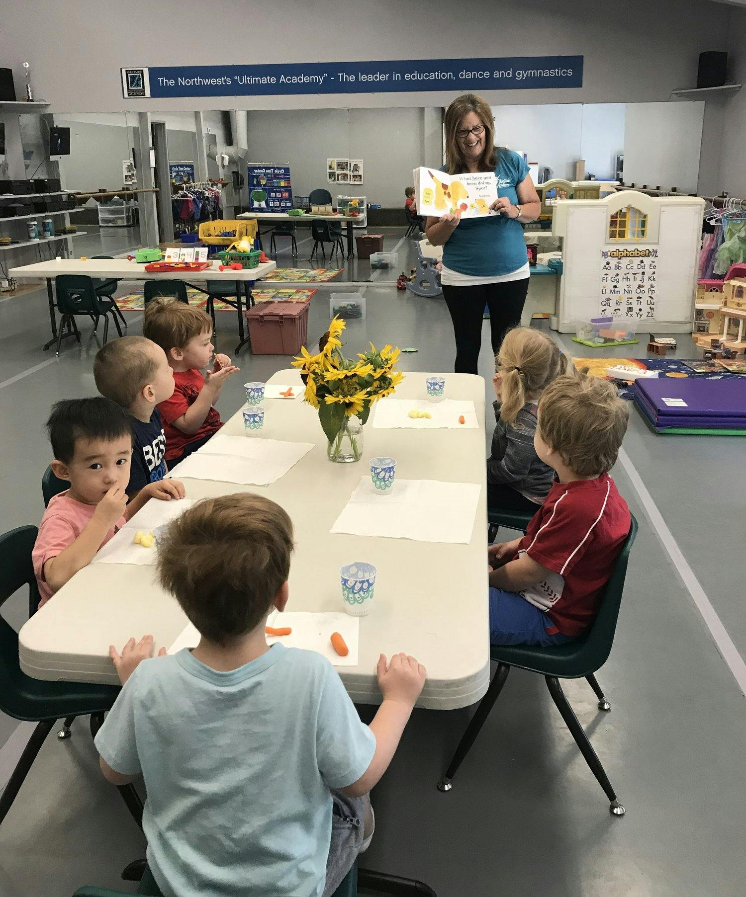 Adult reading a book to children seated at a table in a classroom