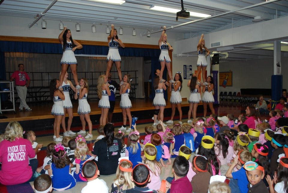 Cheerleaders performing stunts on a stage for an audience of children