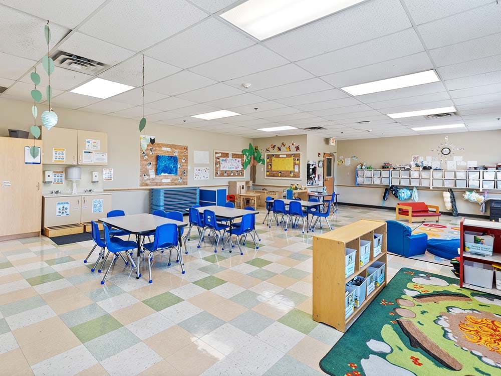 Classroom with small tables and chairs, cubbies, and a play area