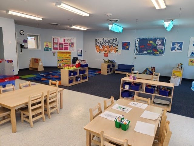An empty children's classroom with small tables and chairs, shelves, and colorful rugs