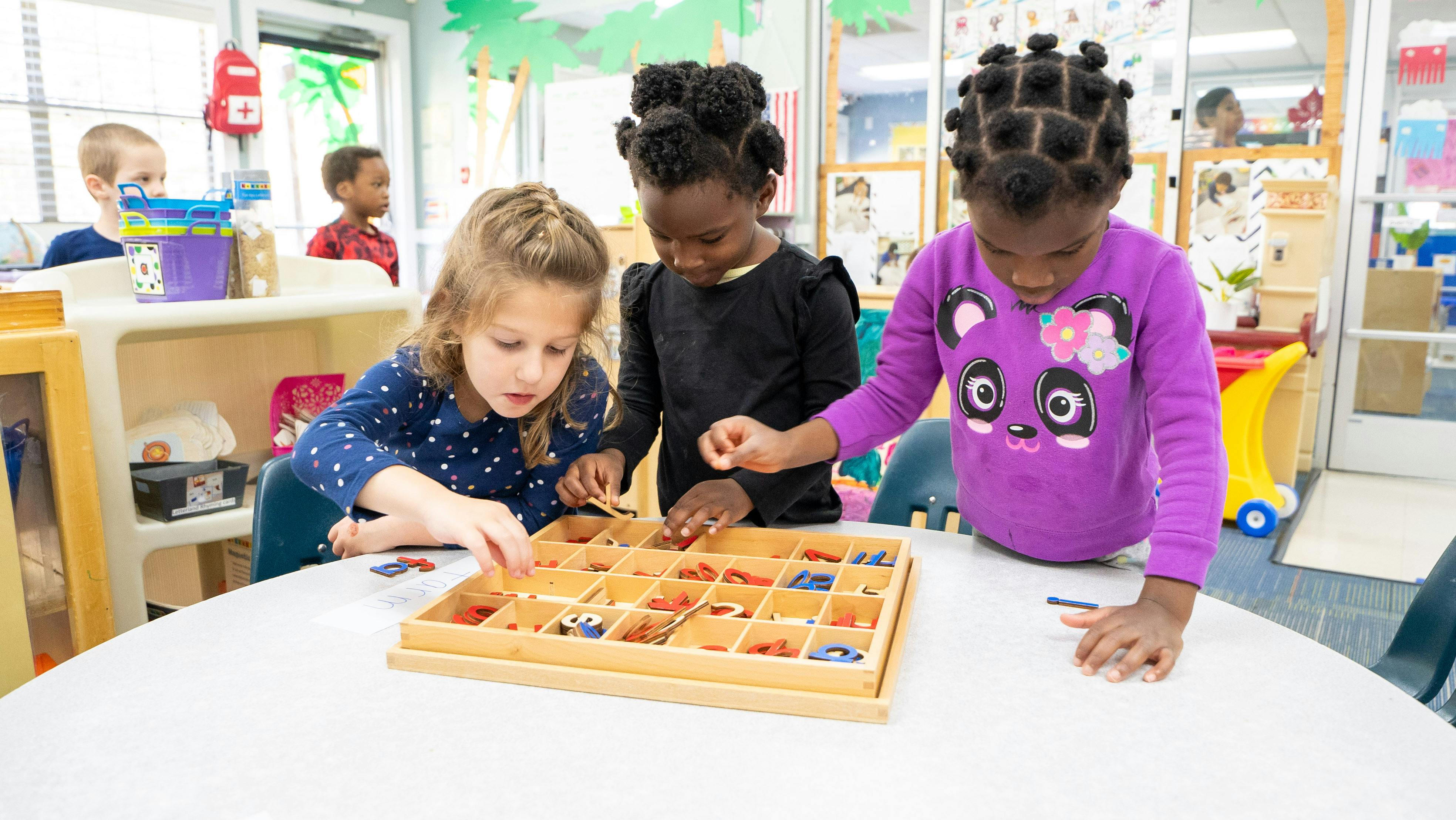 Three children playing with a wooden sorting tray at a table