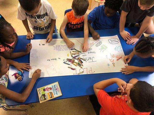 Children drawing on a large piece of paper with crayons at a table